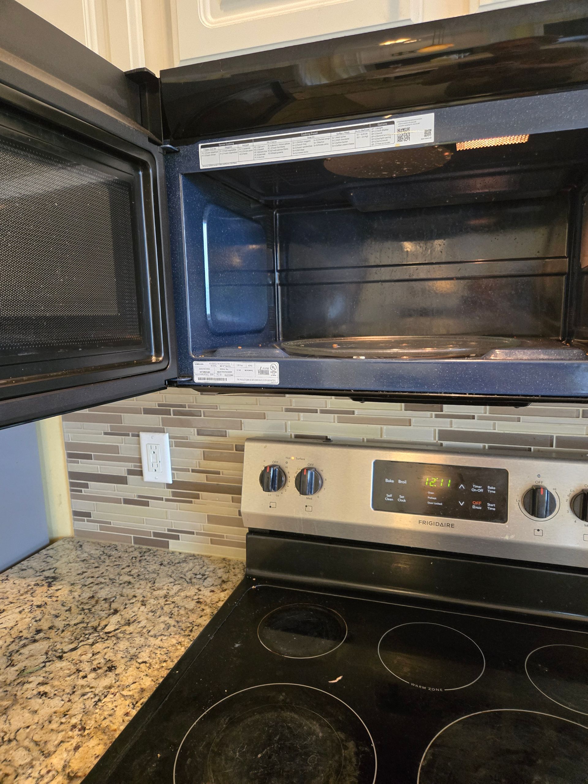 Open microwave above a stovetop, showing the interior. Kitchen setting with tile backsplash.