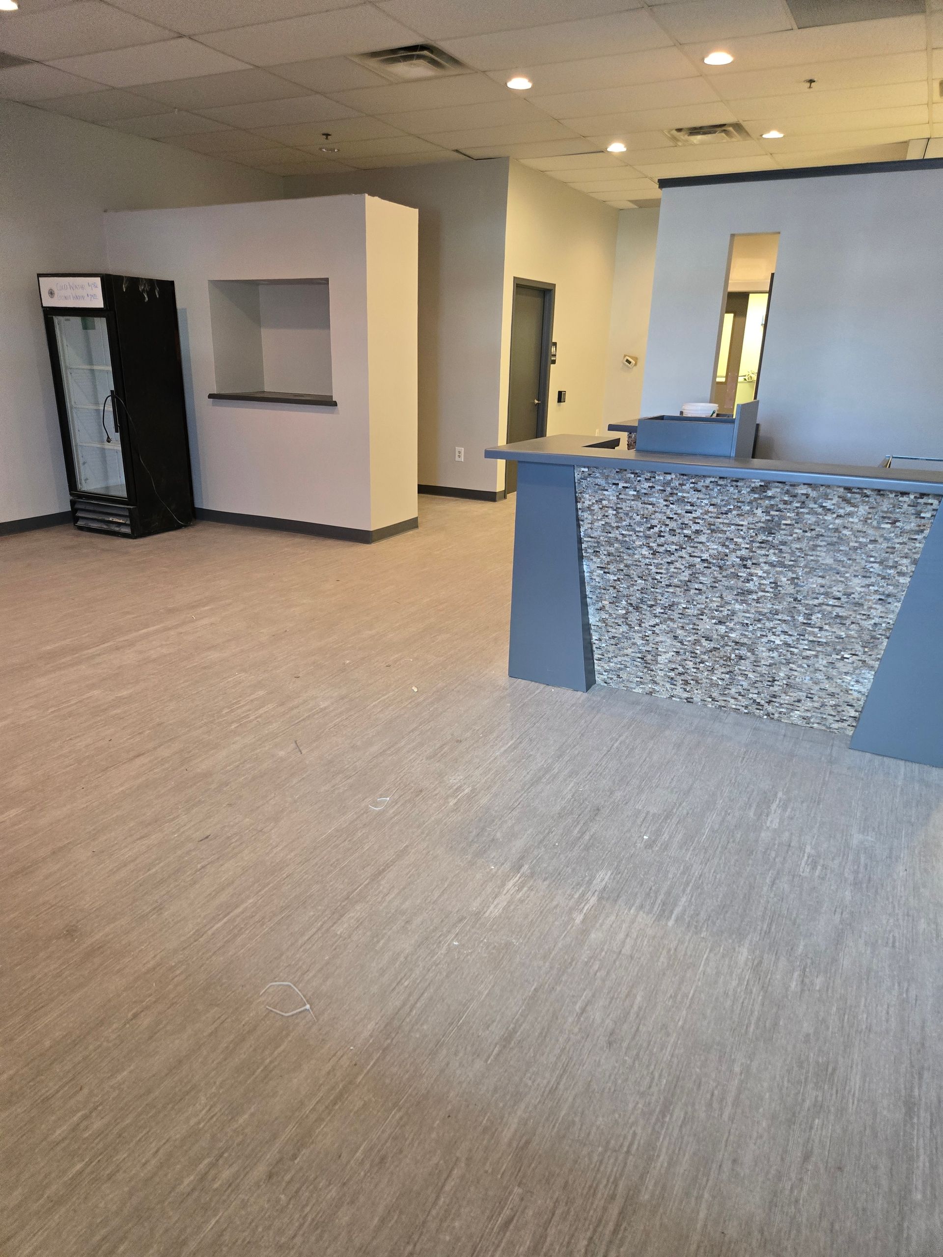 Empty commercial space with counter, drink cooler, and light carpet.
