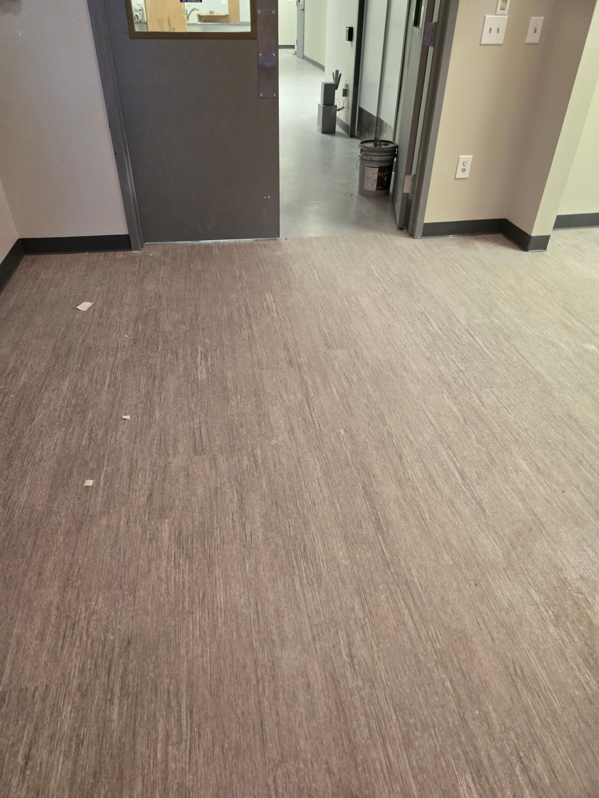 Empty room with gray flooring, a closed gray door, and an open doorway leading to a hallway.