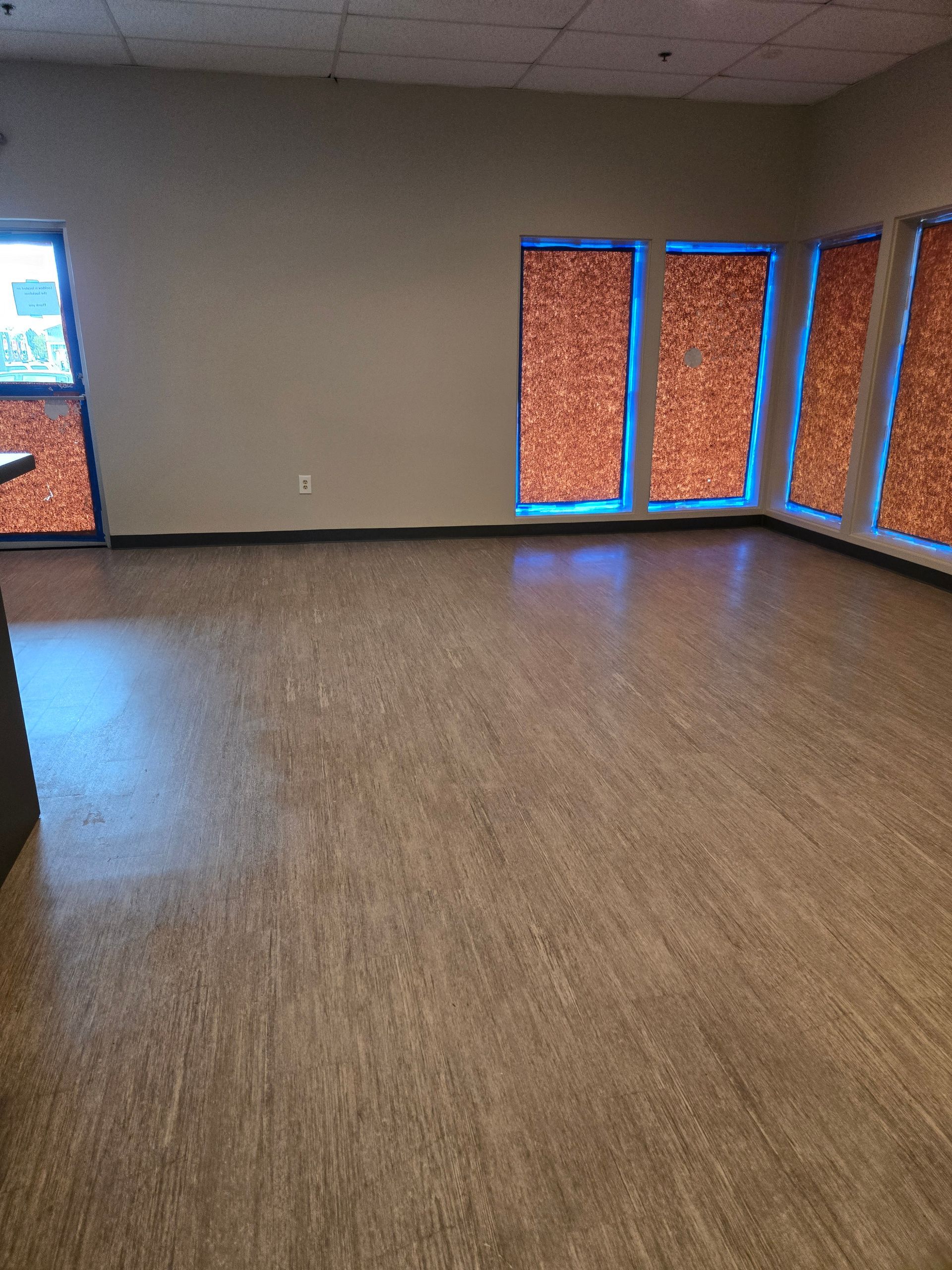 Empty room with beige walls, brown flooring, and windows with orange covering.