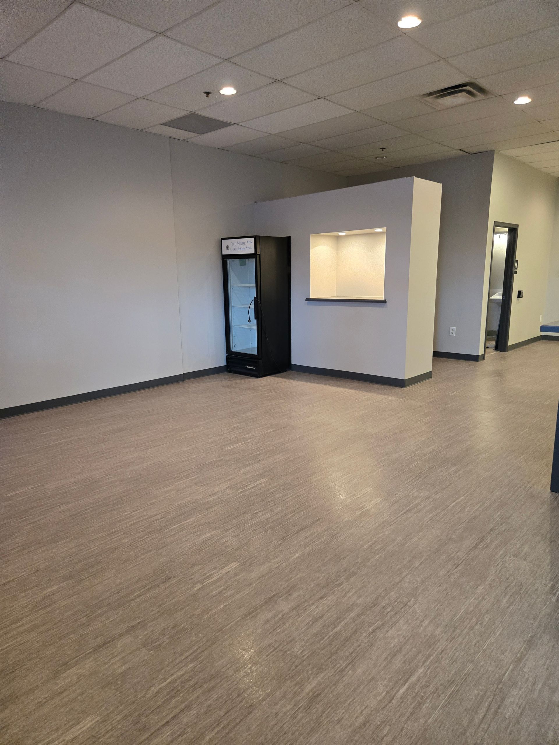 Empty commercial space with neutral walls, flooring, a display refrigerator, and a service counter.