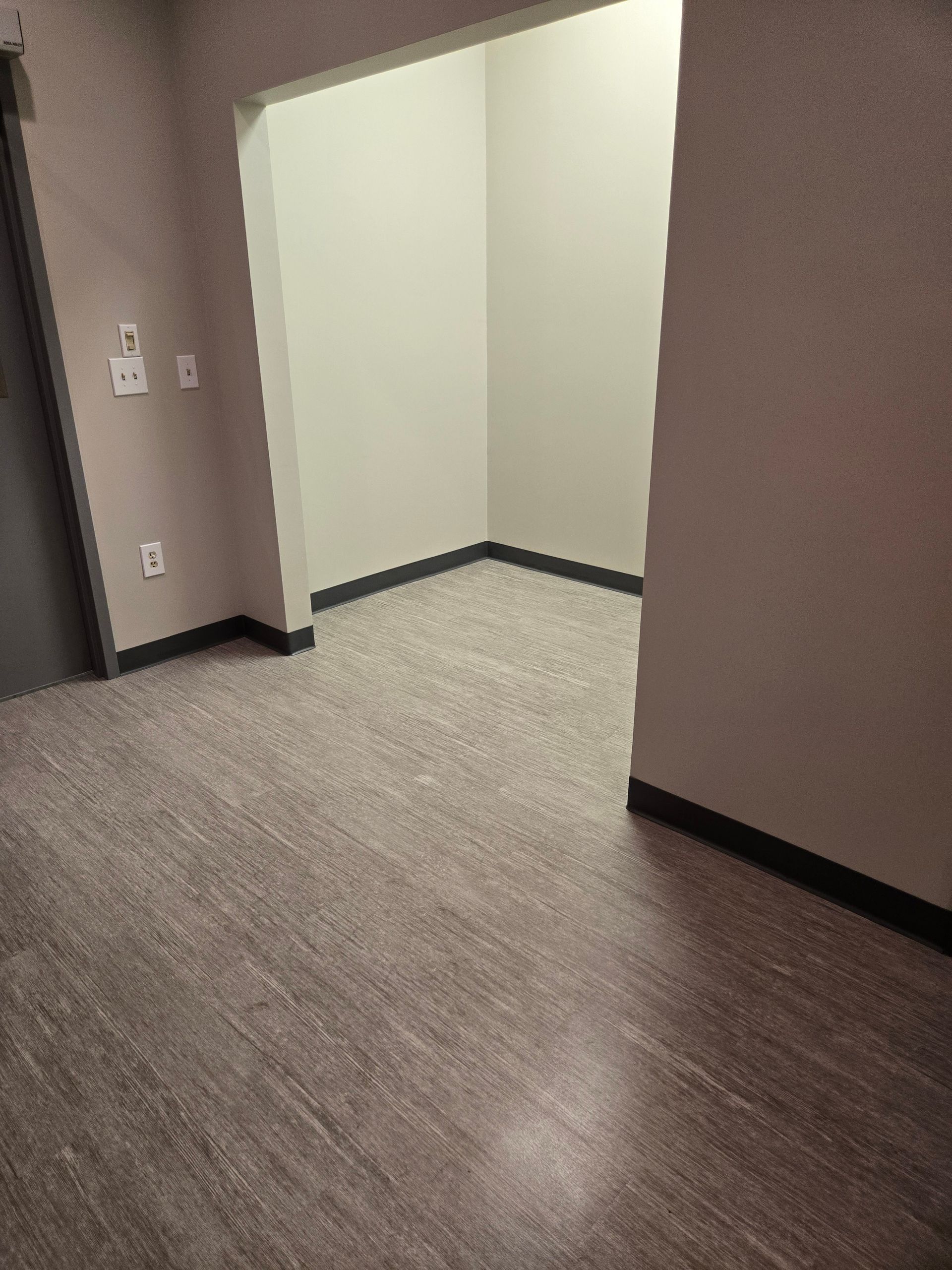 Empty hallway with wood-look flooring and an opening to another room. The walls are light.
