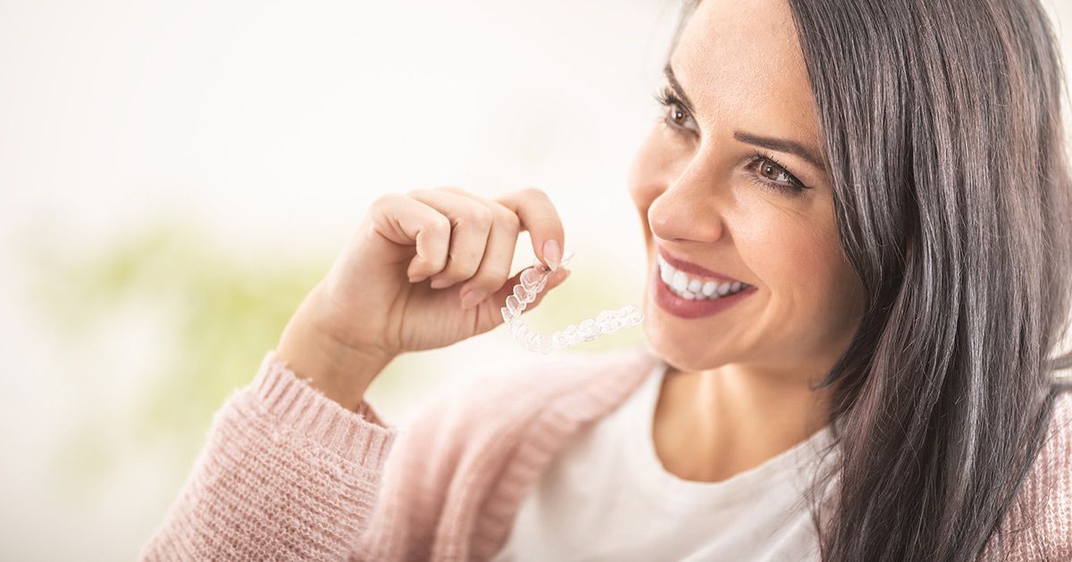 A woman is smiling while holding a clear retainer in her hand.