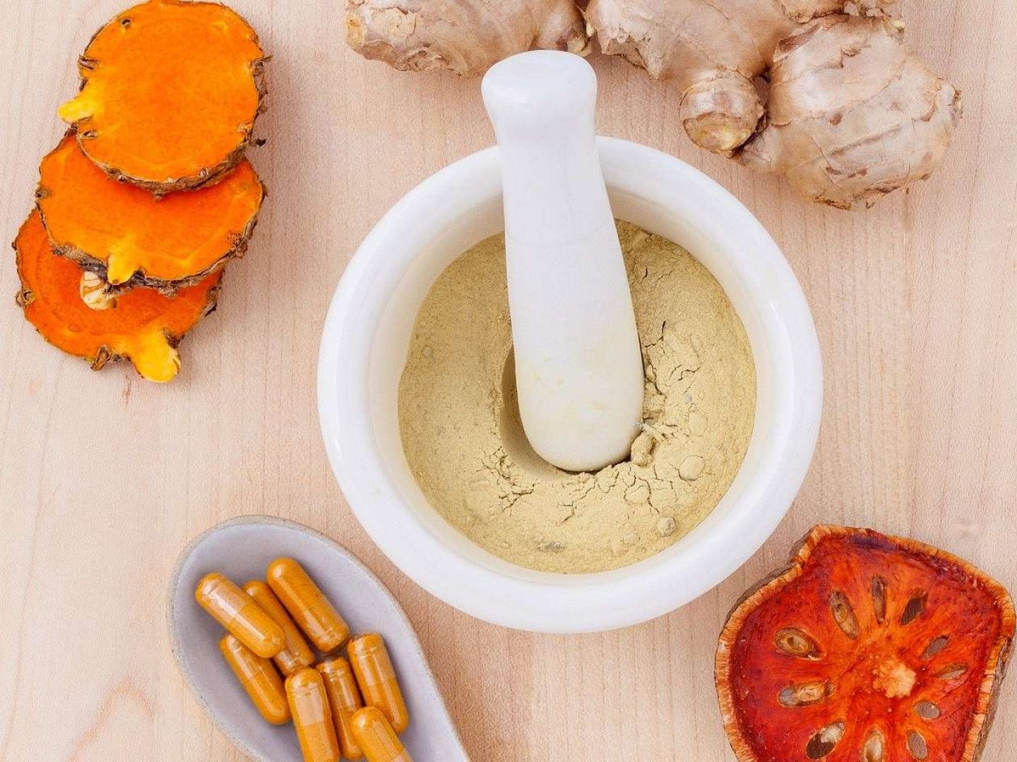 Turmeric, ginger, and other herbal remedies in a mortar, on a wooden surface.