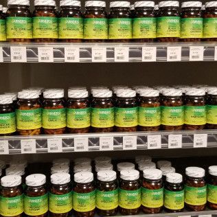 Shelves of supplement bottles with green and white labels in a store.