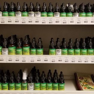 Shelves of small glass bottles with green and white labels, possibly supplements or essential oils.