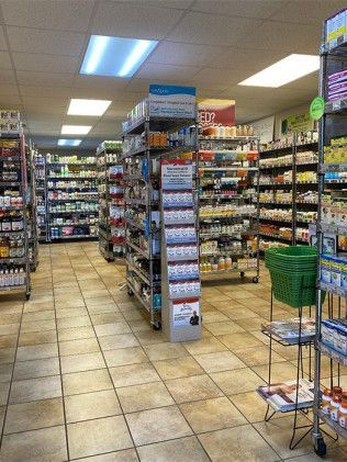 Inside a health food store: shelves of products, aisle with a display, tiled floor, overhead lighting.