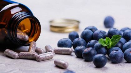 Brown bottle with pills spilling onto a surface, alongside a pile of fresh blueberries.
