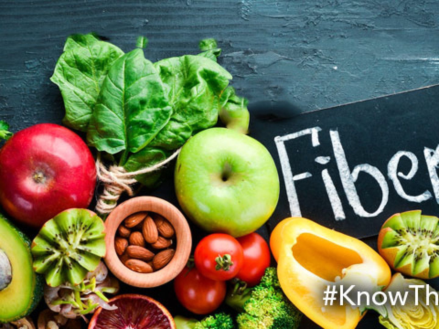 Fresh fruits and vegetables including apples, avocado, and spinach arranged with a sign that says 