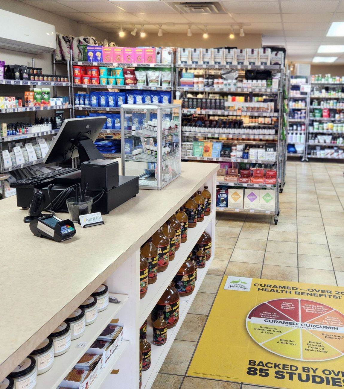 Woman smiling, eating berries from a white bowl with a spoon. Kitchen setting, wearing gray hoodie and green shirt.