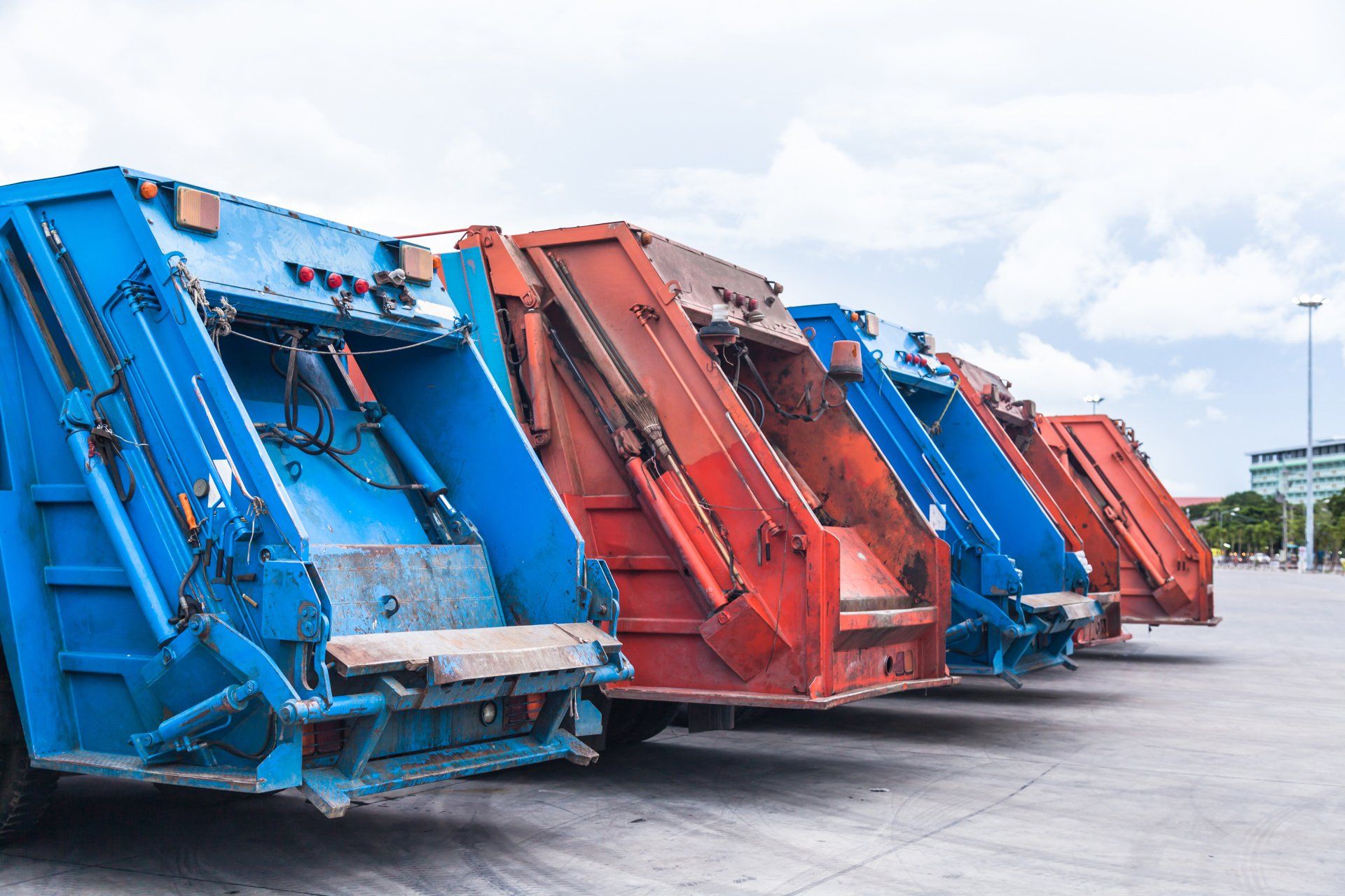 A row of garbage trucks are parked in a parking lot.