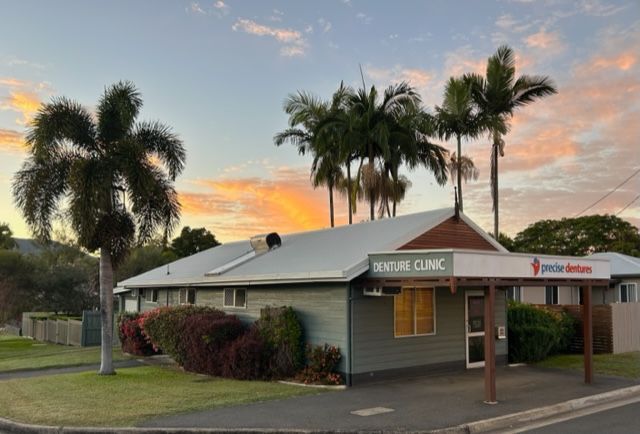 A small building with palm trees in front of it and a sunset in the background-Denture Care in Berserker, QLD