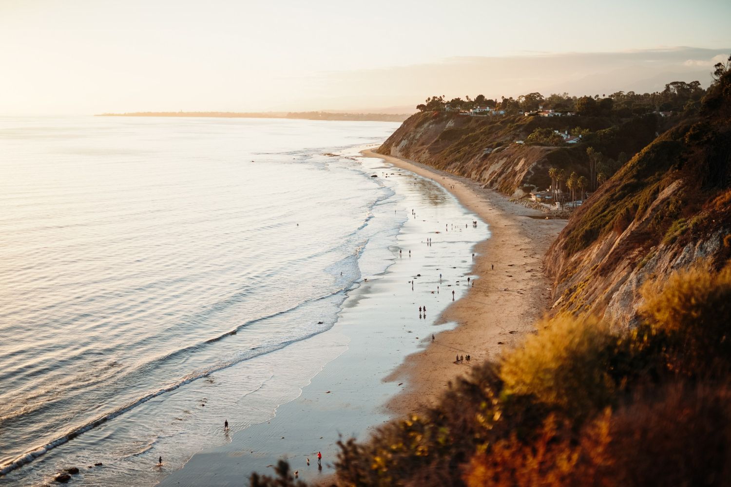 Sunset over a curving beach with calm waves and a coastal cliff