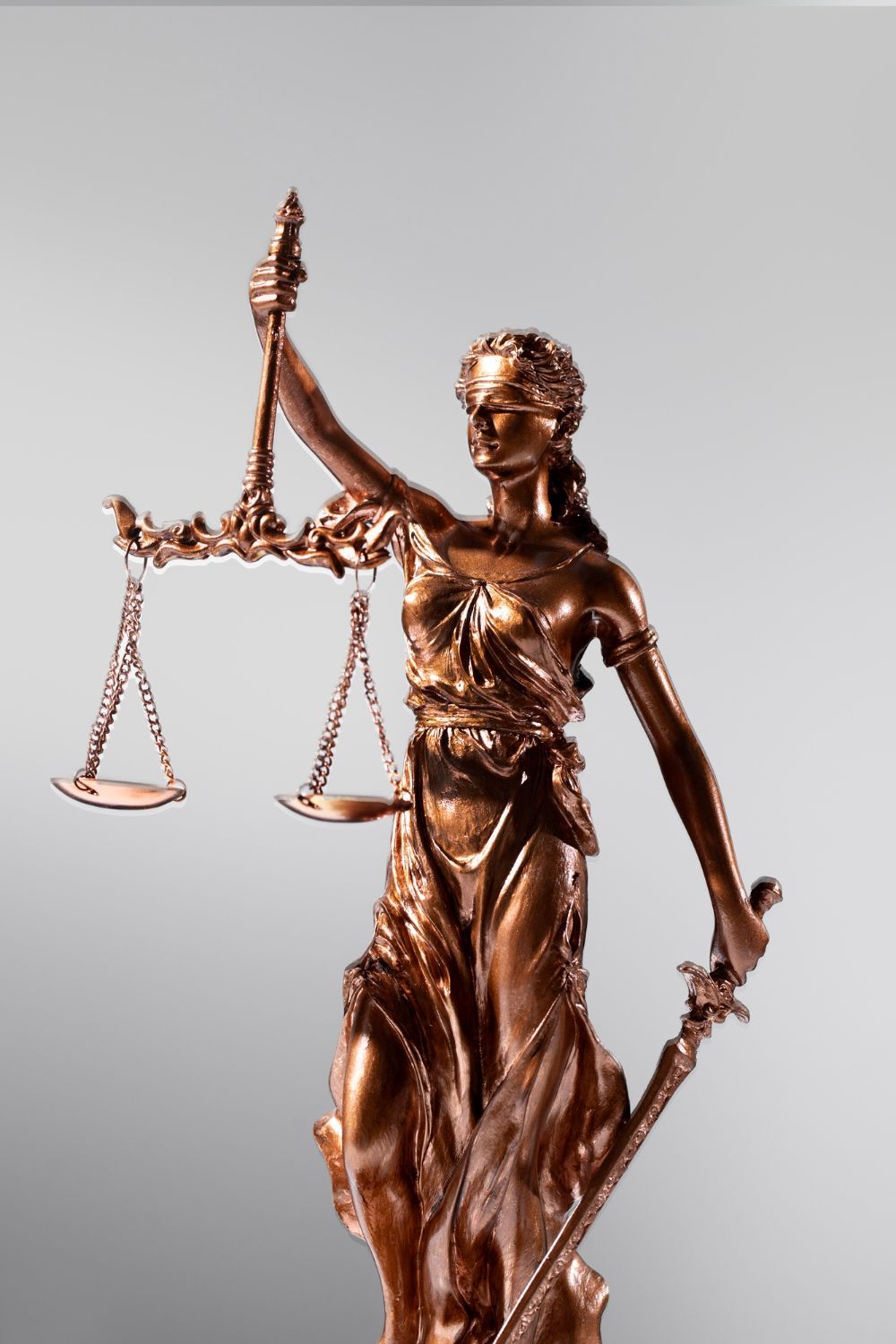 Bronze Lady Justice statue holding scales and a sword on a gray background