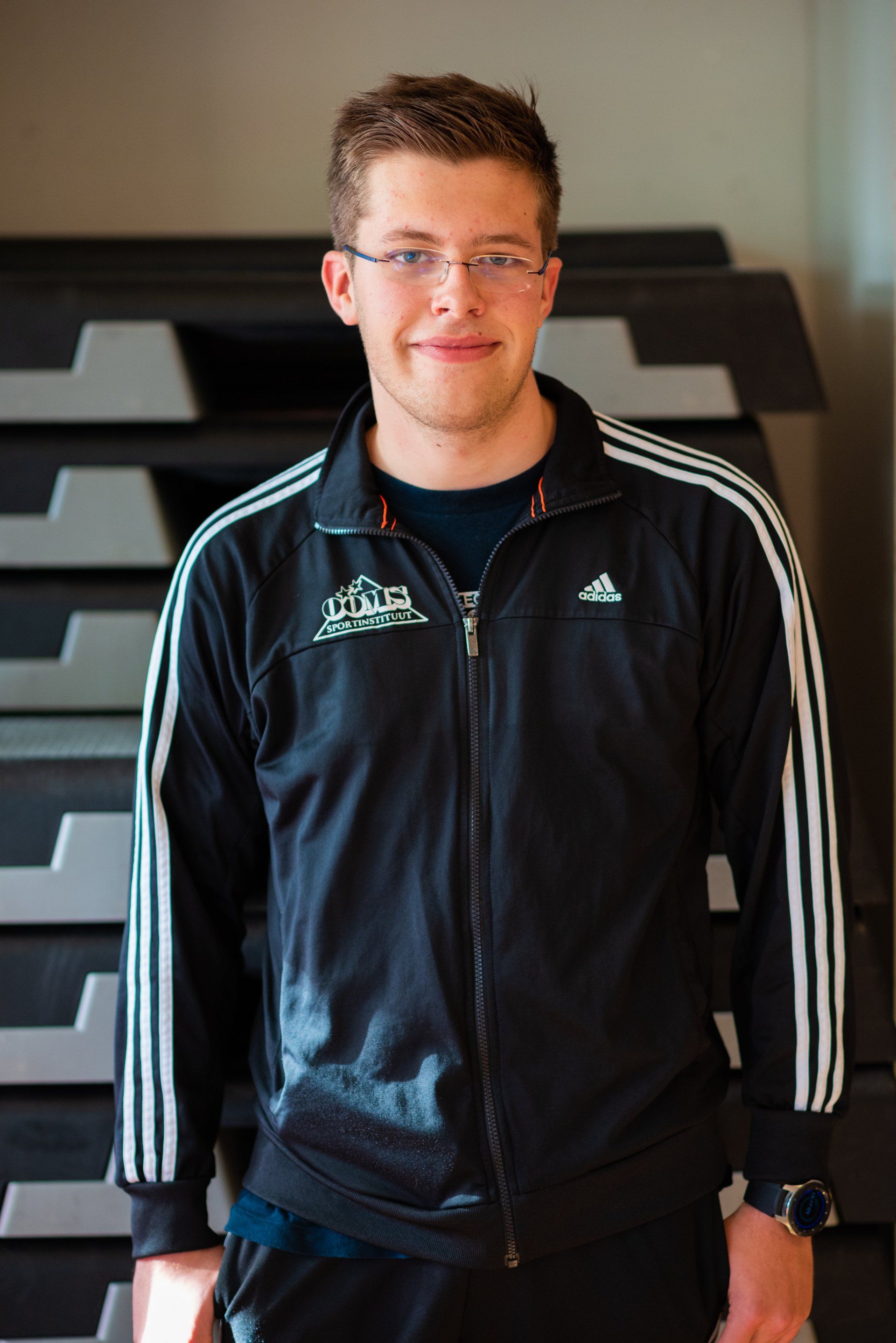 Voor een stapel trappen staat een man in een zwart adidas-jack.