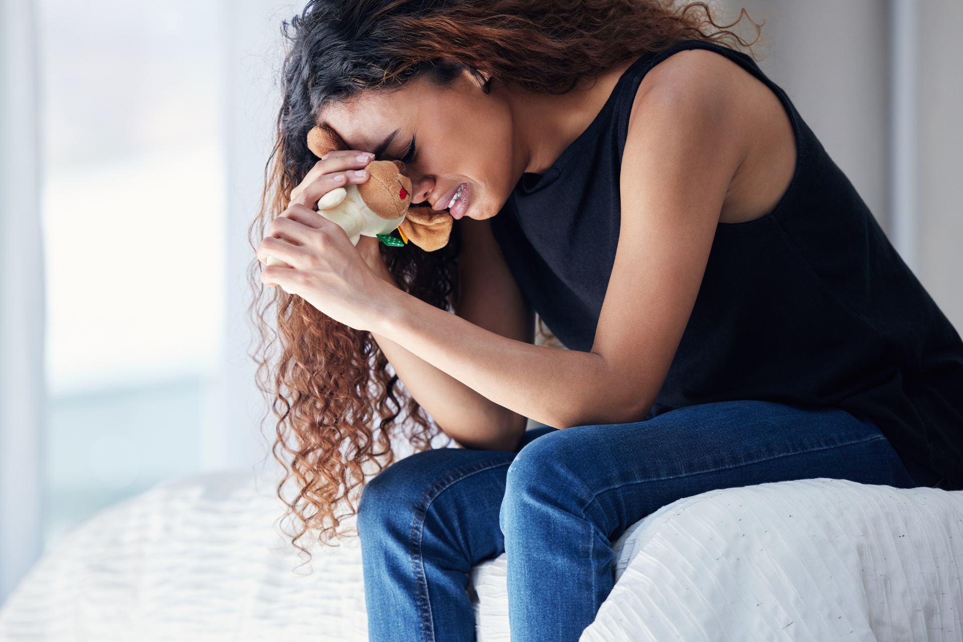 Woman sitting on a bed, looking down and holding a pill bottle, appearing distressed.