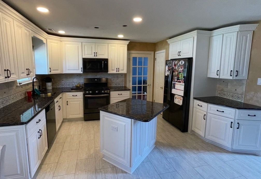 A kitchen with white cabinets , stainless steel appliances , hardwood floors and a large island.