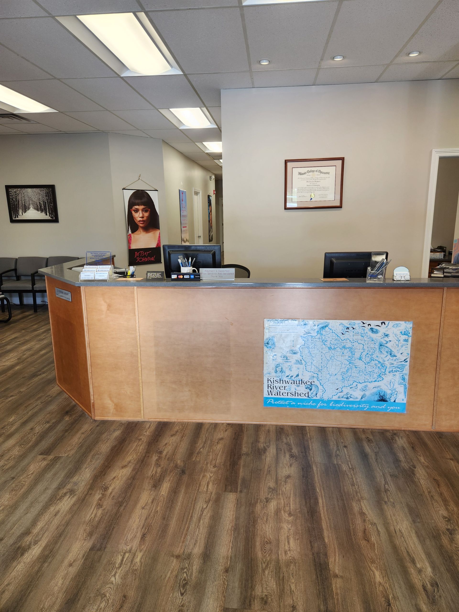 Reception area with wooden desk, computers, and artwork; waiting area with chairs and a hallway.