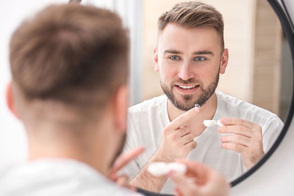 Man in white shirt looking at mirror, putting in contact lens.