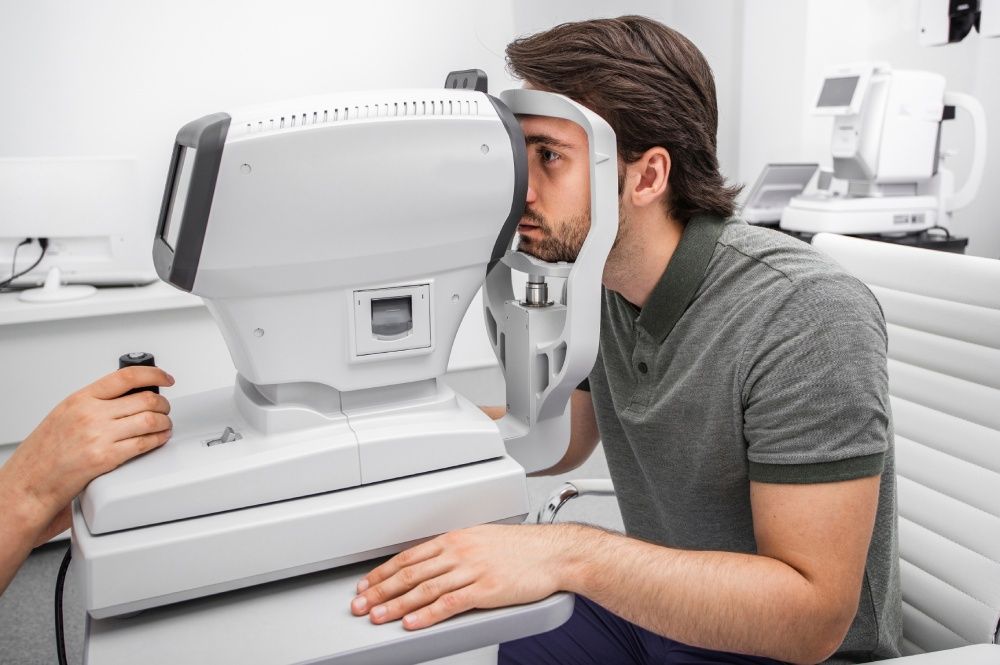 Man undergoing eye exam with medical equipment. Person's eye in focus, doctor using controls in white clinic.