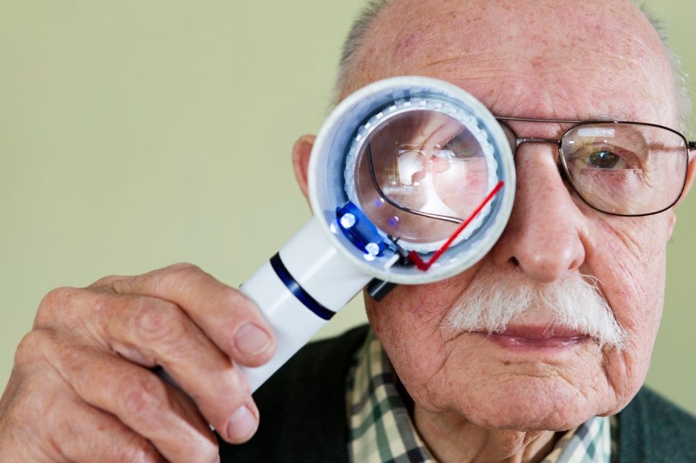Elderly man looking through a large magnifying glass at a watch.