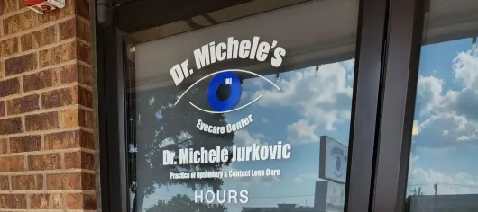 Sign on a glass door for Dr. Michele's eye care practice, featuring an eye graphic and the doctor's name.