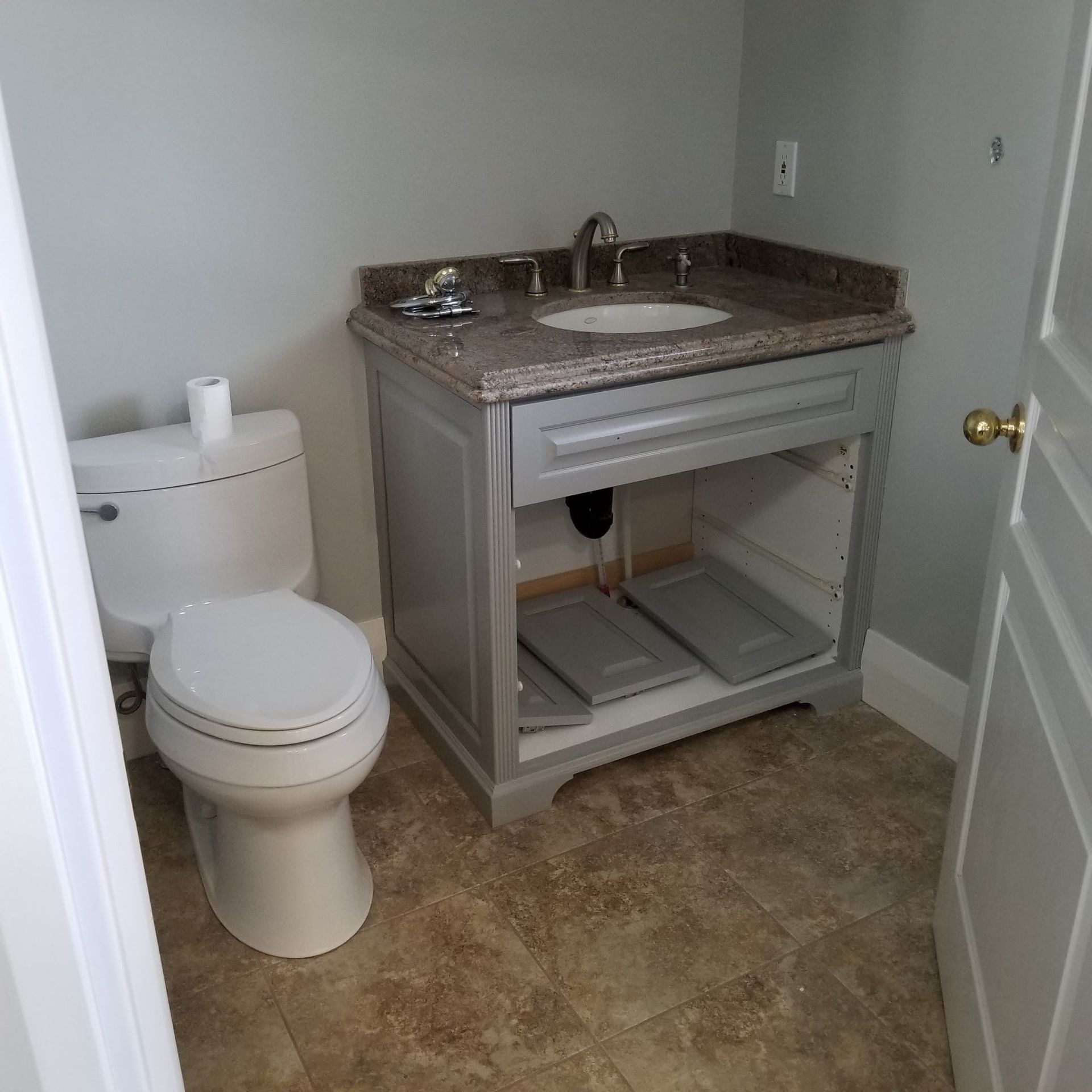 Bathroom with gray vanity, toilet, and tan floor. Gray walls.