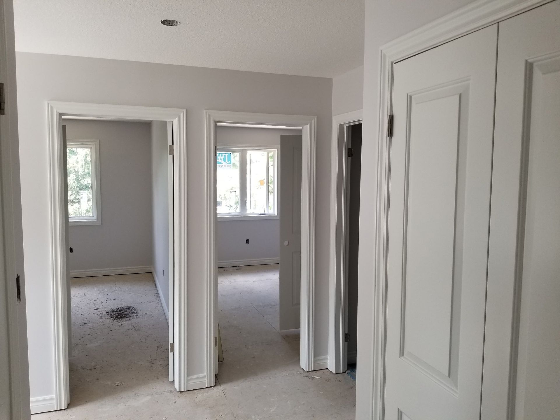 Hallway with three doorways, two to bedrooms with windows, one to a closet. White trim, gray walls.