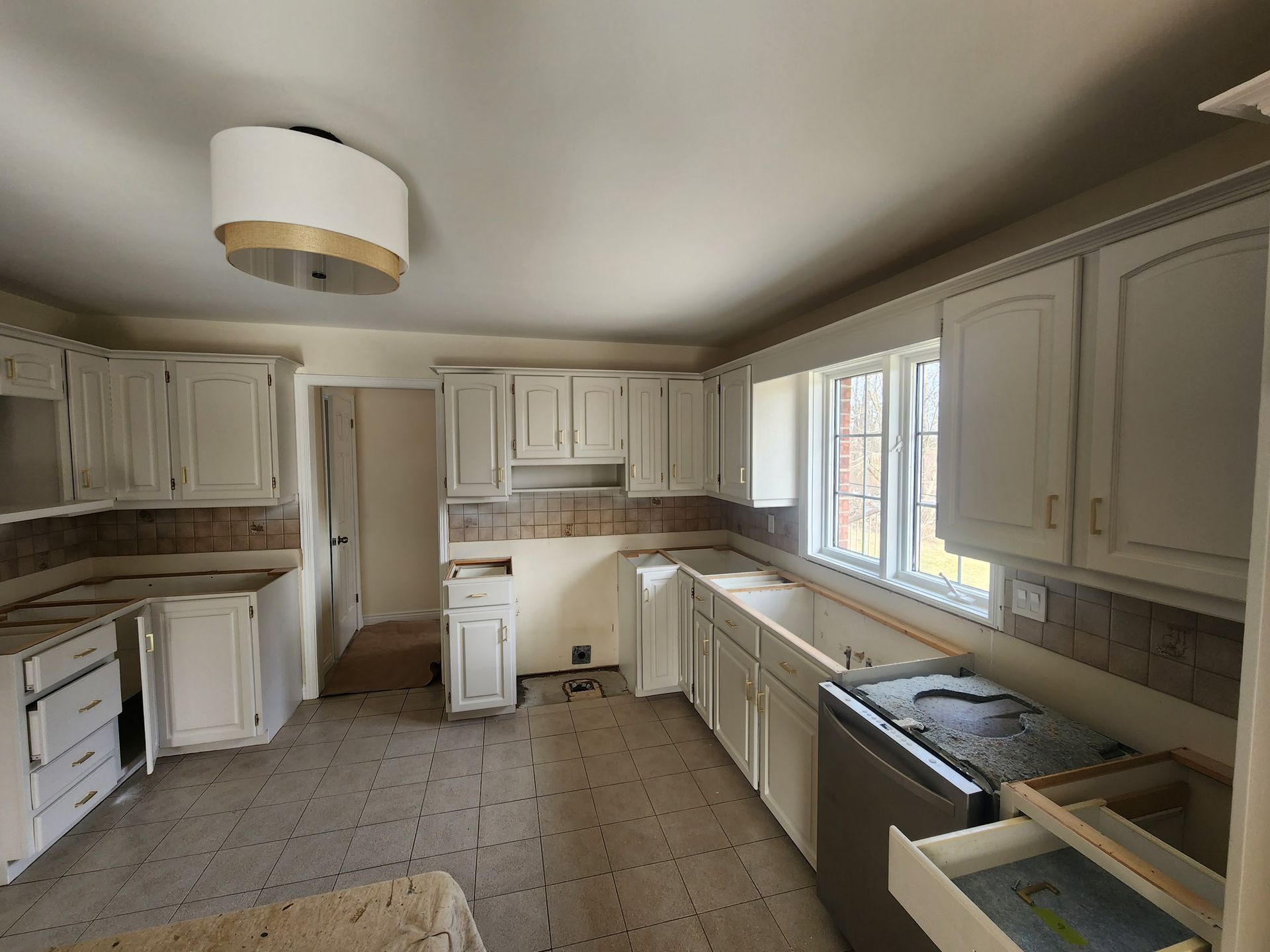 Kitchen undergoing renovation with white cabinets, beige tile backsplash, and light fixture.