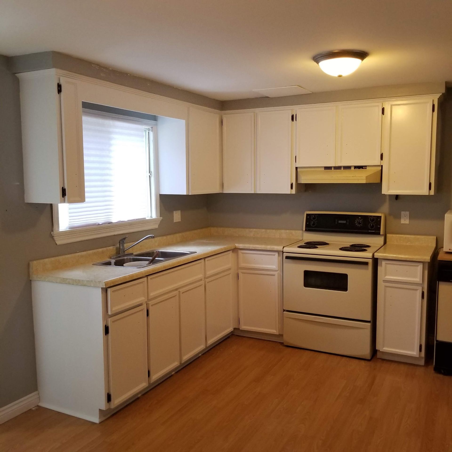 White kitchen cabinets and appliances in a room with a window, countertop, and wood floor.