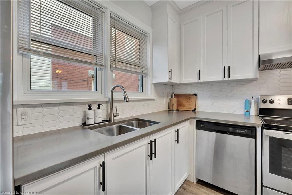 White kitchen with stainless steel appliances, grey countertops, and window blinds.