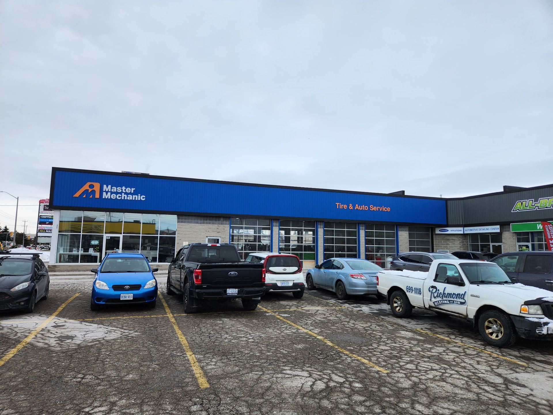 Auto repair shop exterior with cars parked in front under a cloudy sky.