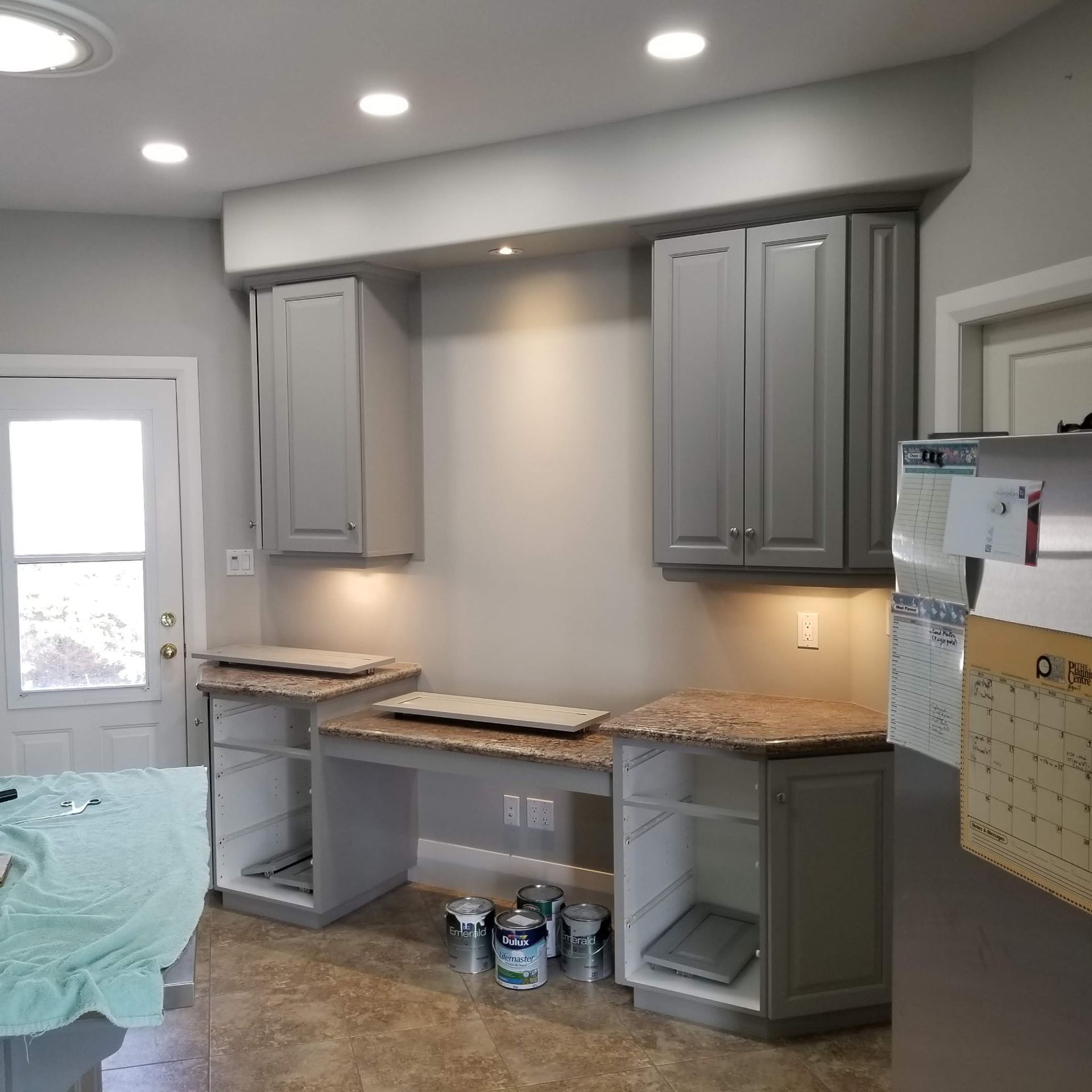 Gray kitchen cabinets with a countertop and paint cans on the floor.