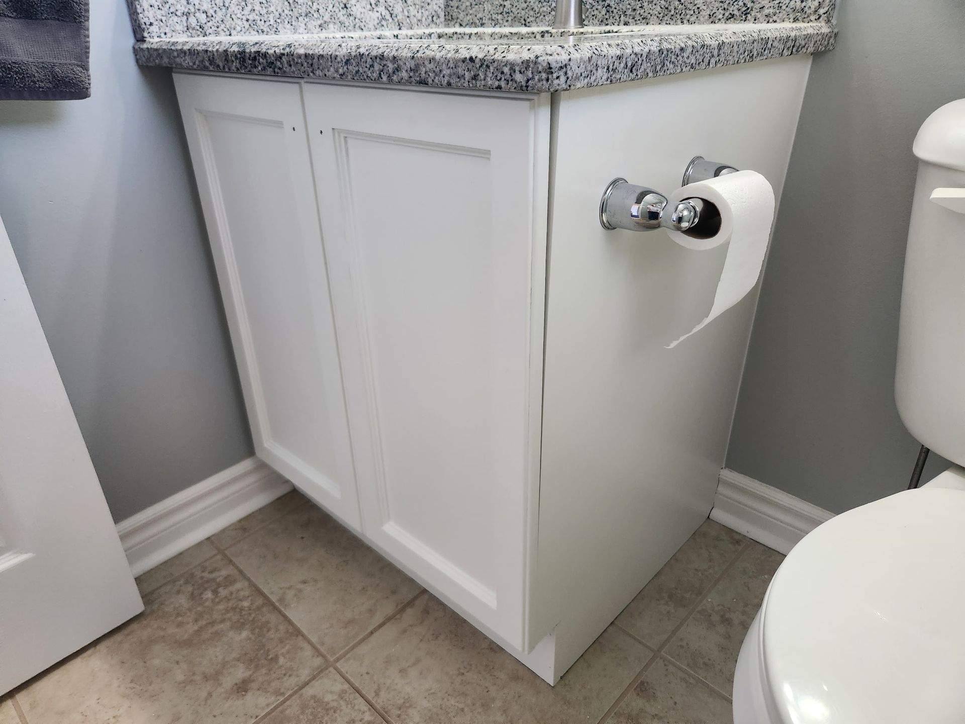 White bathroom cabinet with granite countertop, toilet, and a roll of toilet paper.