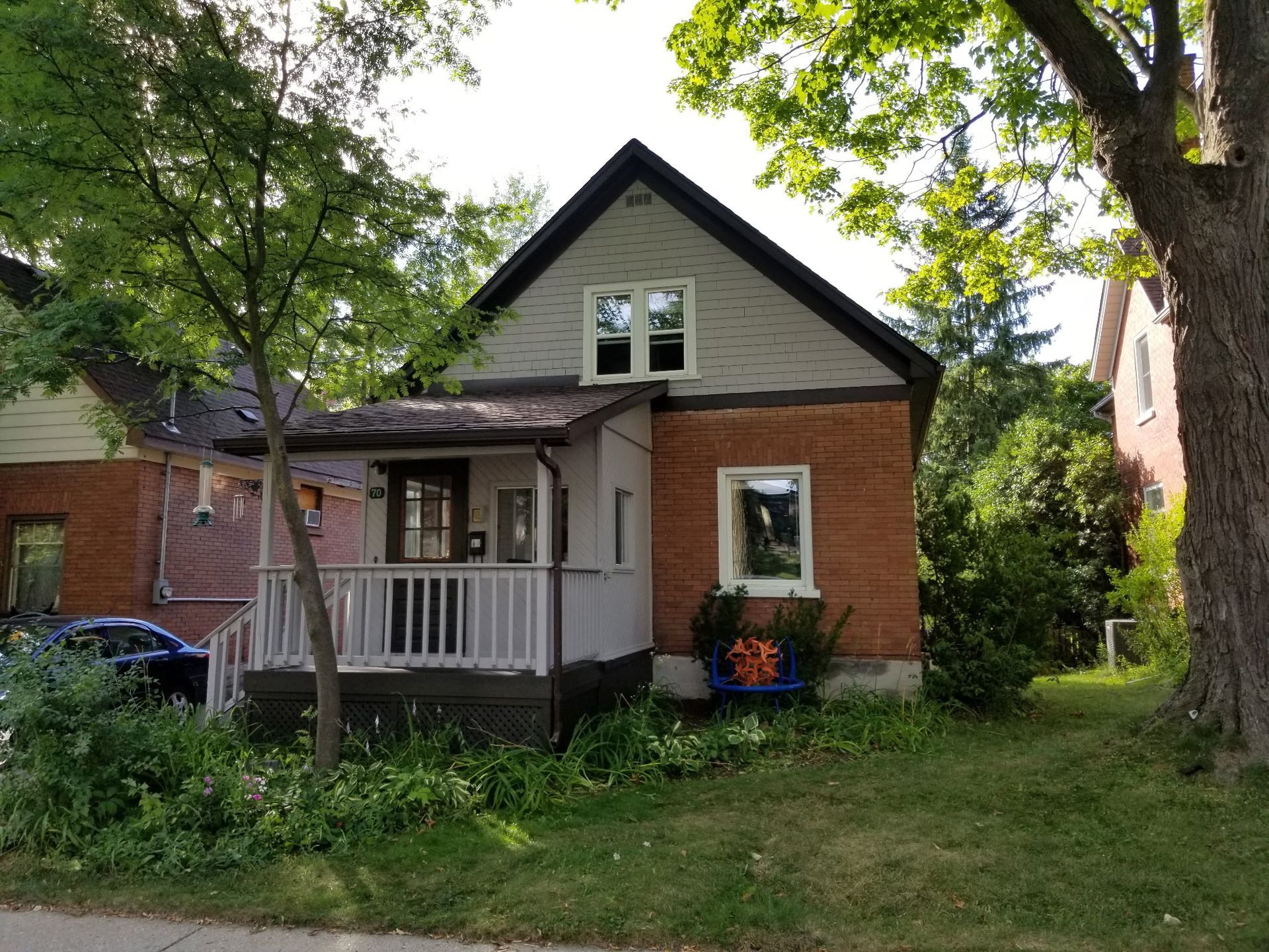 Two-story brick house with a small porch, surrounded by greenery.