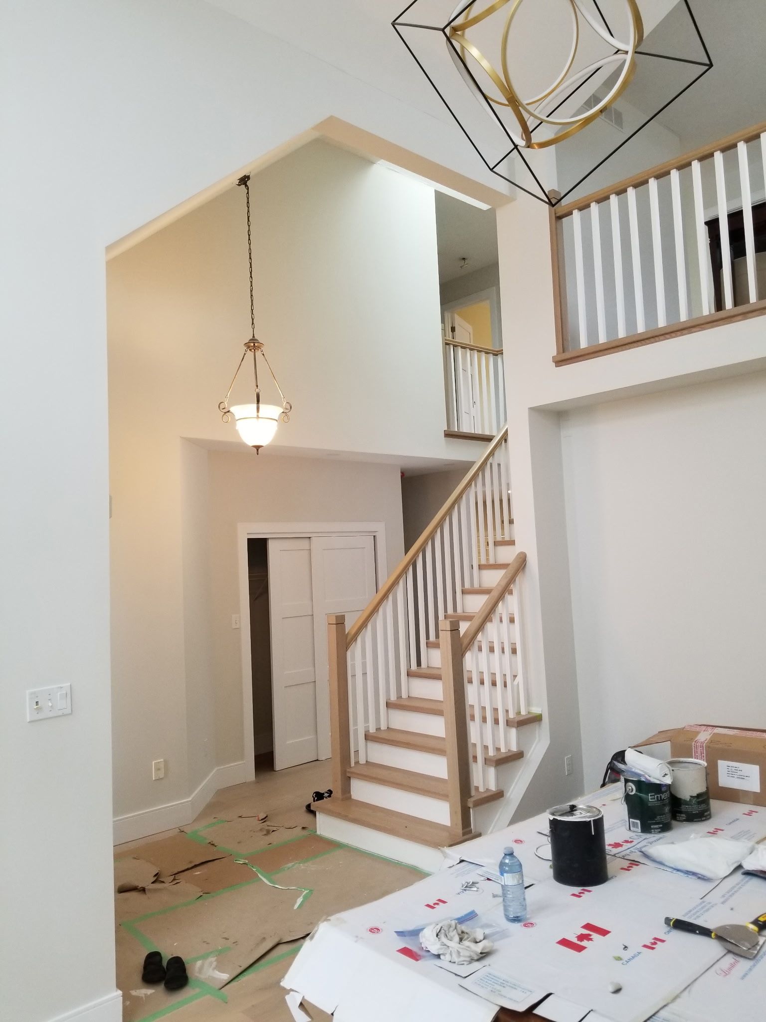 Interior view of a two-story home with staircase, chandelier, and a loft area. White and light wood details.