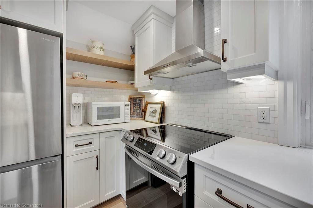 Small white kitchen with stainless steel appliances, white cabinets, and light wood shelving.