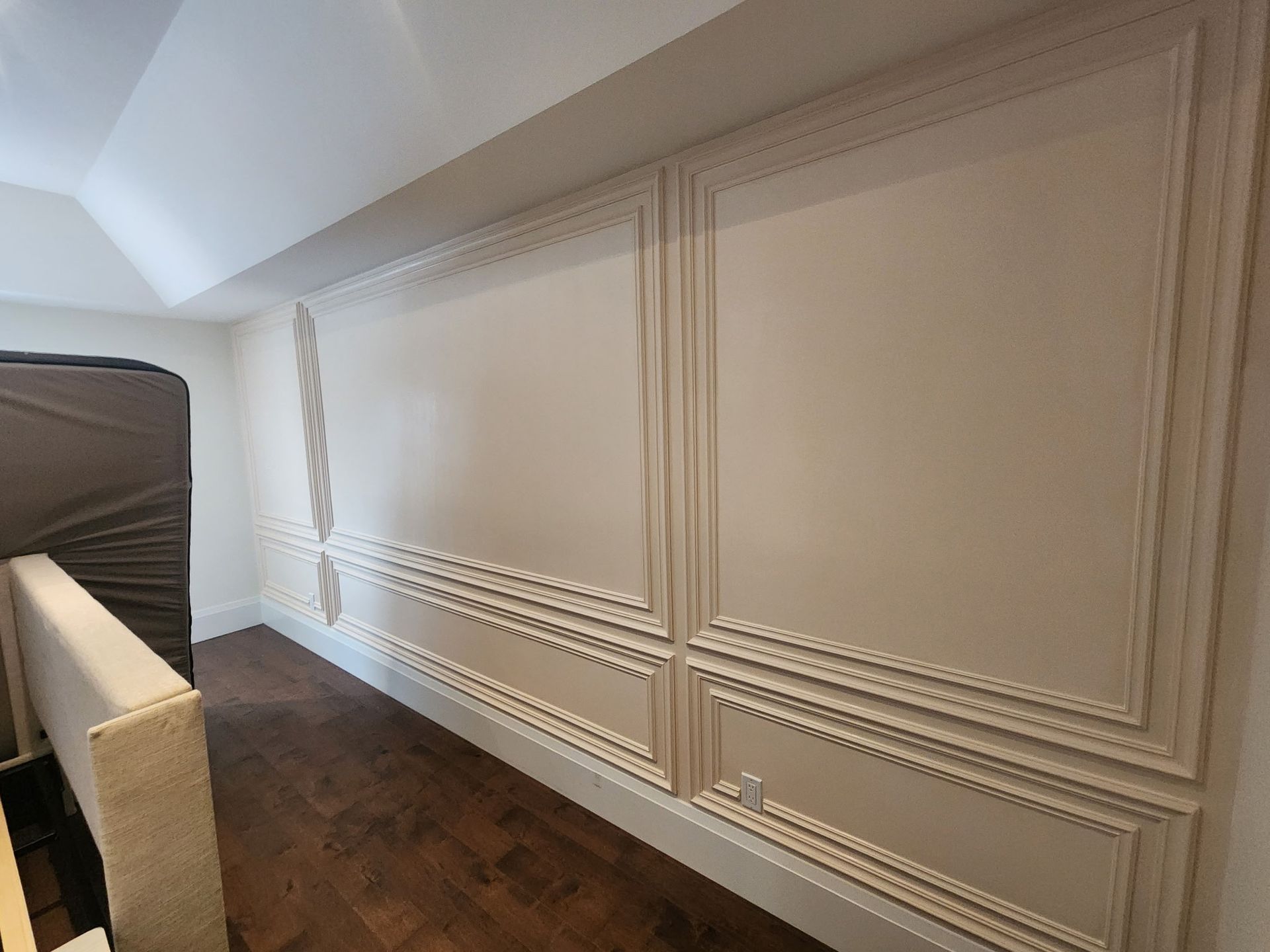 Cream-colored wall paneling with decorative trim. A dark wood floor is below, with a slanted ceiling above.