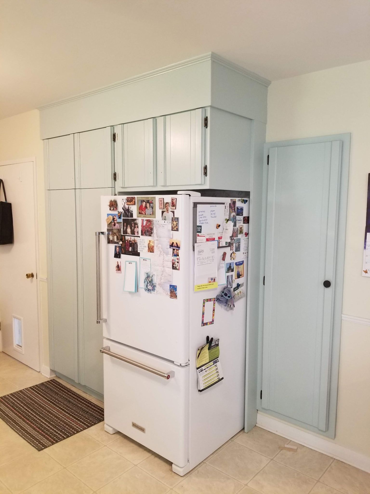 Refrigerator surrounded by light blue cabinets in a kitchen, with a matching door to the right.