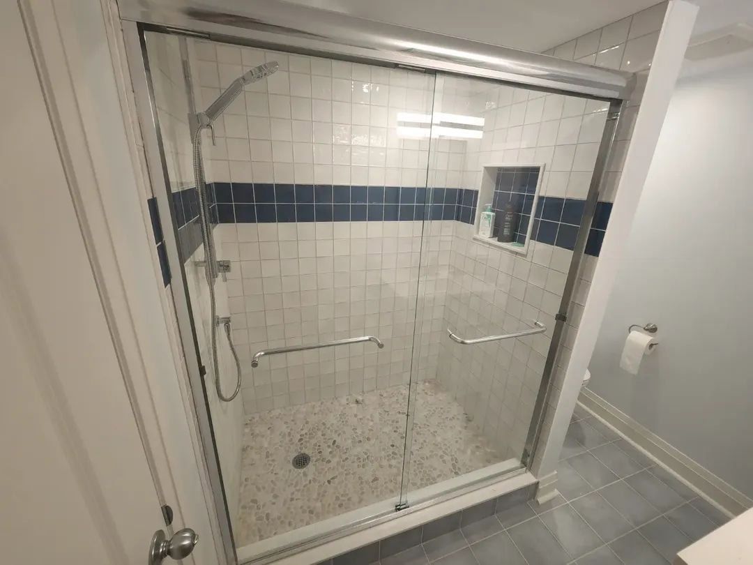 Shower stall with glass doors, white and blue tiled walls, and pebble floor.
