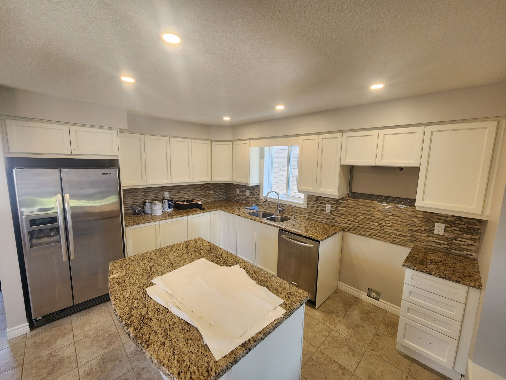 White kitchen with granite countertops, stainless steel appliances, and island.