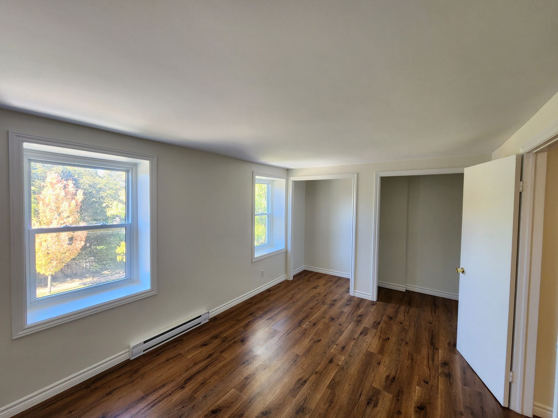Empty bedroom with two windows, two closets, and hardwood floor.