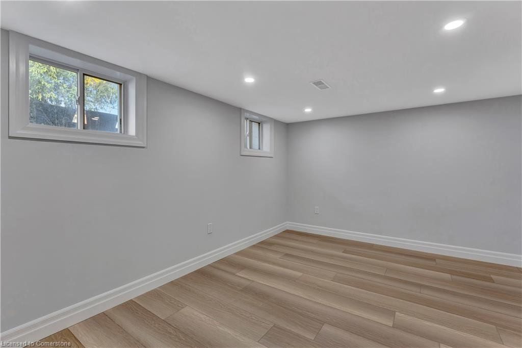 Empty room with light gray walls, wooden floor, two windows, and recessed lighting.