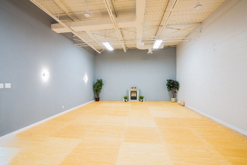 Empty yoga studio with light wooden floor, gray and white walls, potted plants.