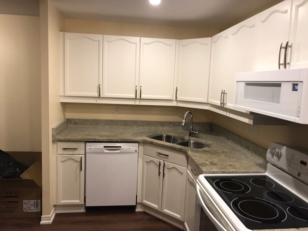 White kitchen cabinets, granite countertop, dishwasher, sink, and stovetop in a corner layout.