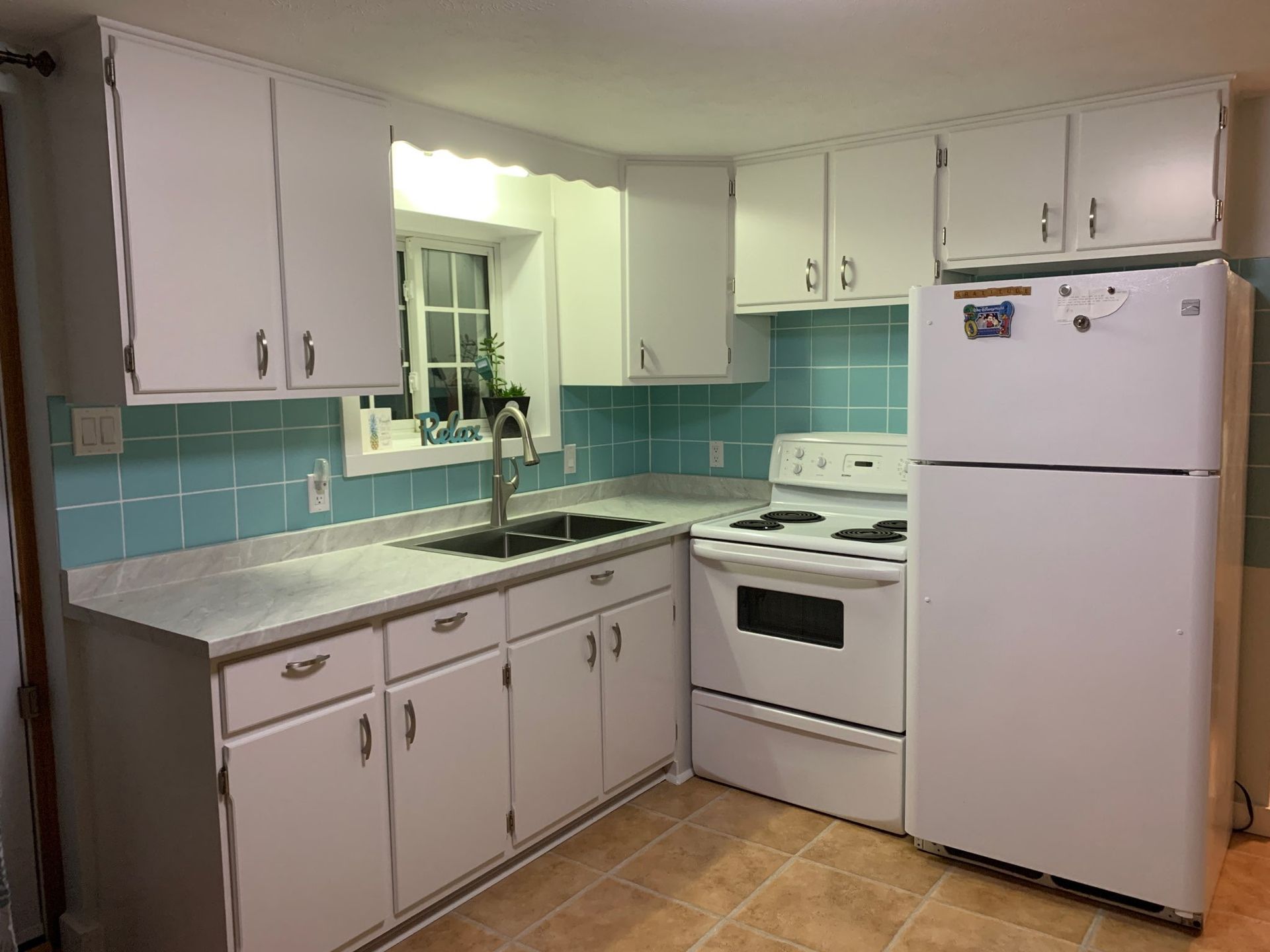 White kitchen with blue tiled backsplash, white appliances and cabinets, and light countertops.