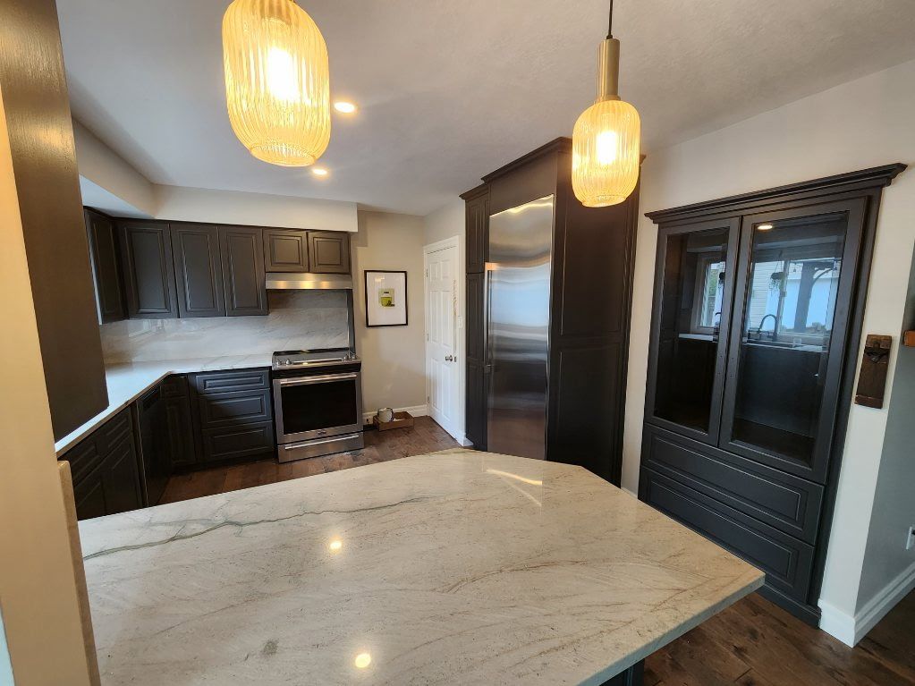 Modern kitchen with dark cabinetry, stainless steel appliances, and a light granite island.