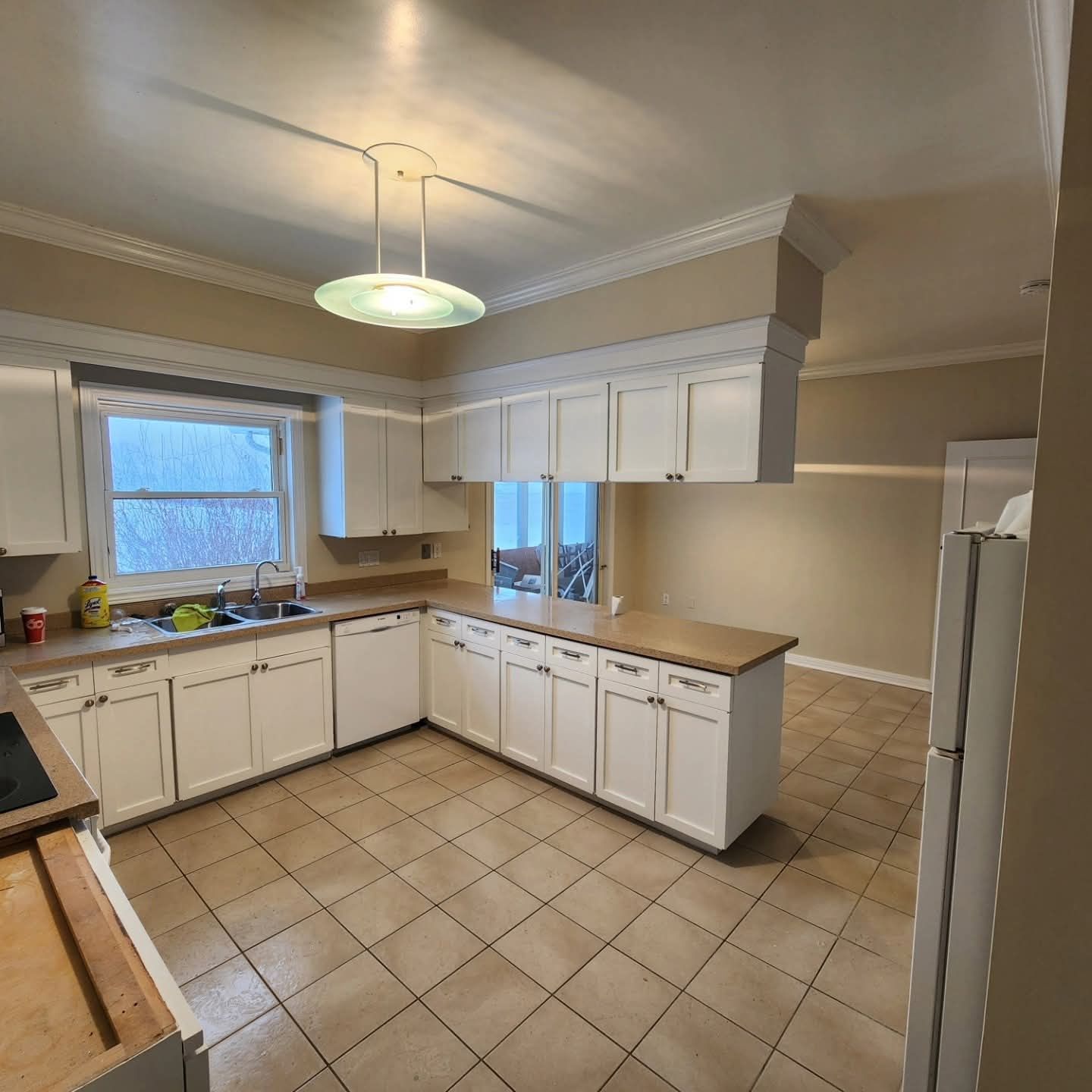 White kitchen with countertops, cabinets, and a tile floor. A window is in the back and a fridge to the right.