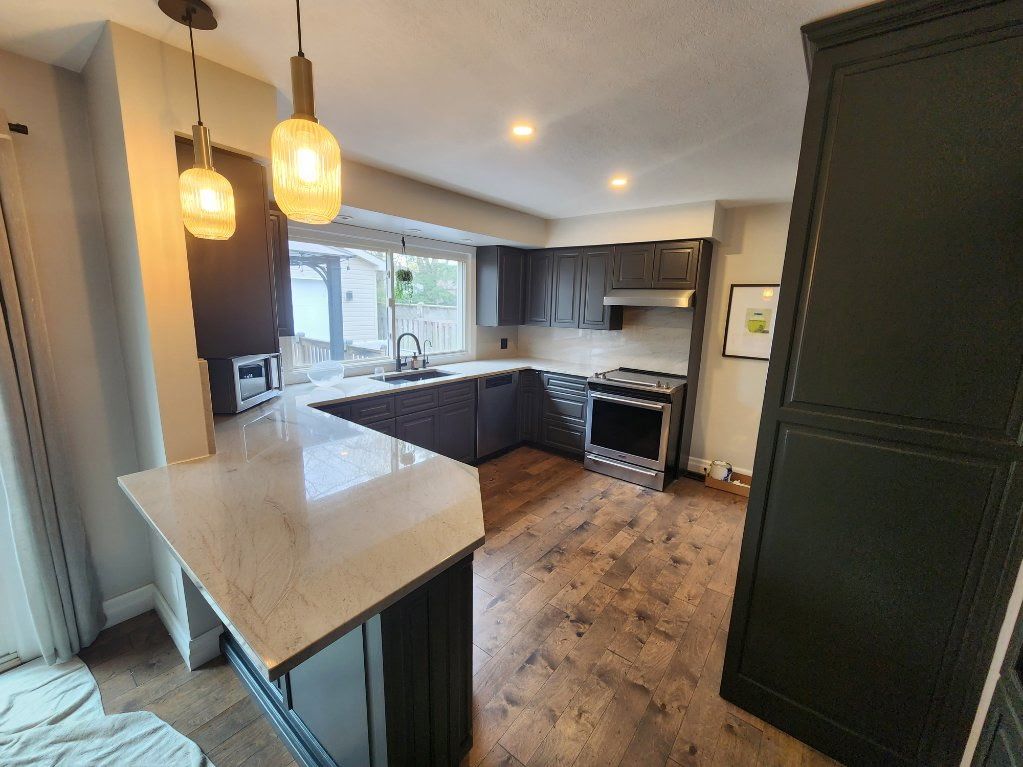Dark gray kitchen with light-colored countertops, hardwood flooring, and two pendant lights.
