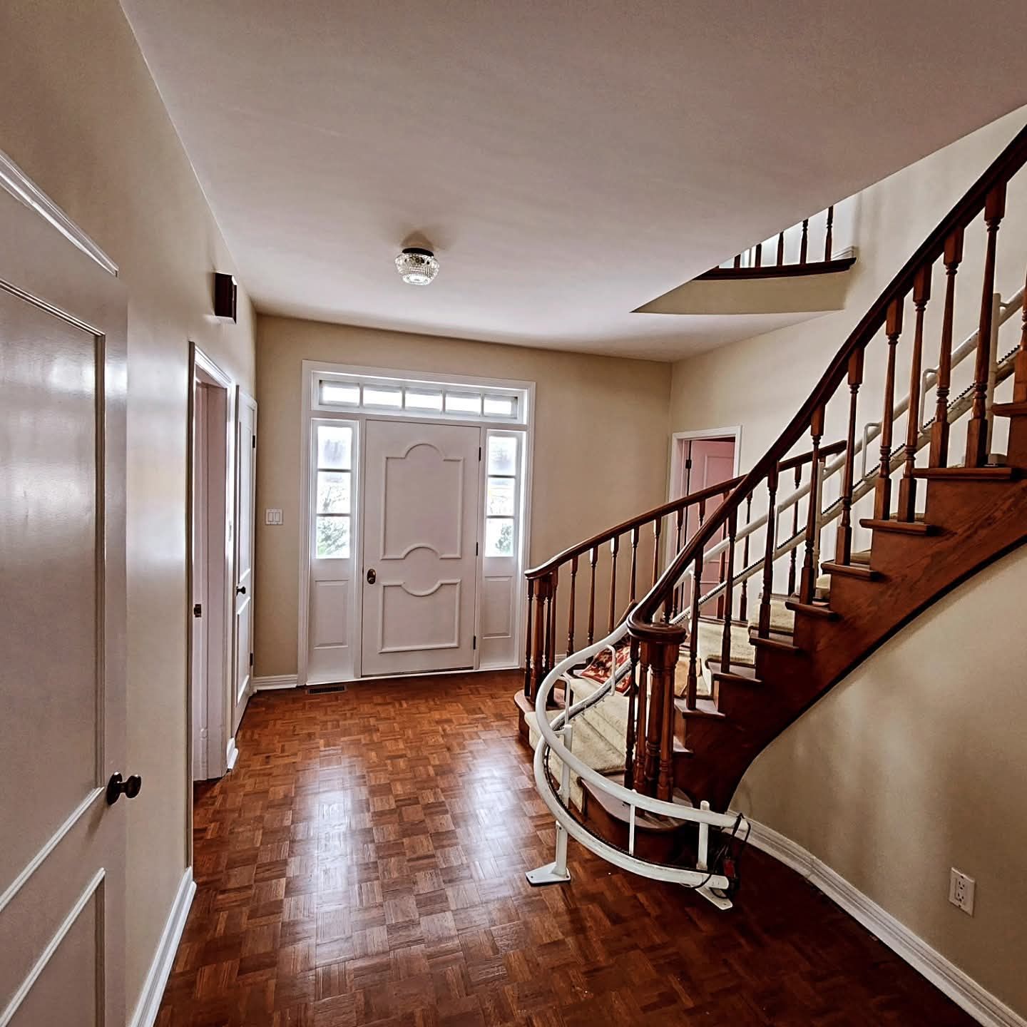 Hallway with wooden staircase, front door, and parquet flooring.